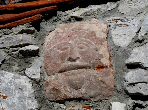 Une pierre gravée qui représente un visage, scellée dans le mur d'une des cabanes.