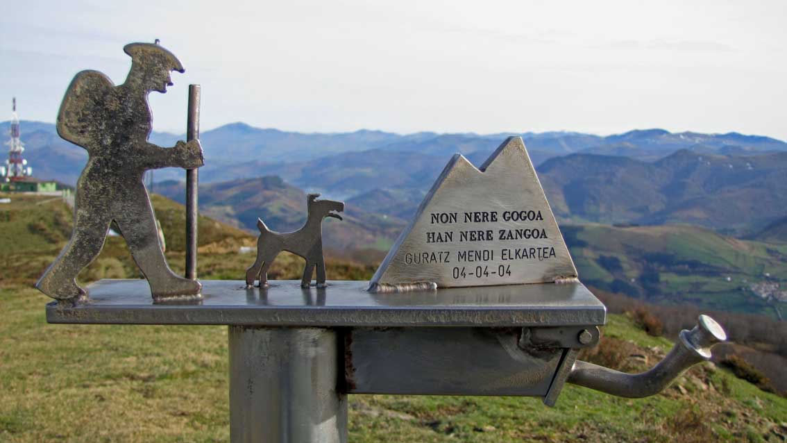 Une sculpture métallique représentant un randonneur accompagné de son chien.